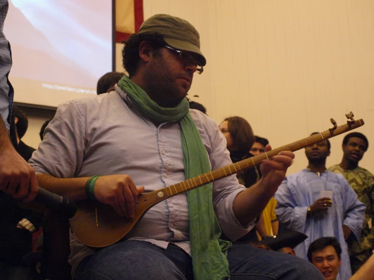 a man sitting in front of a crowd holding a guitar