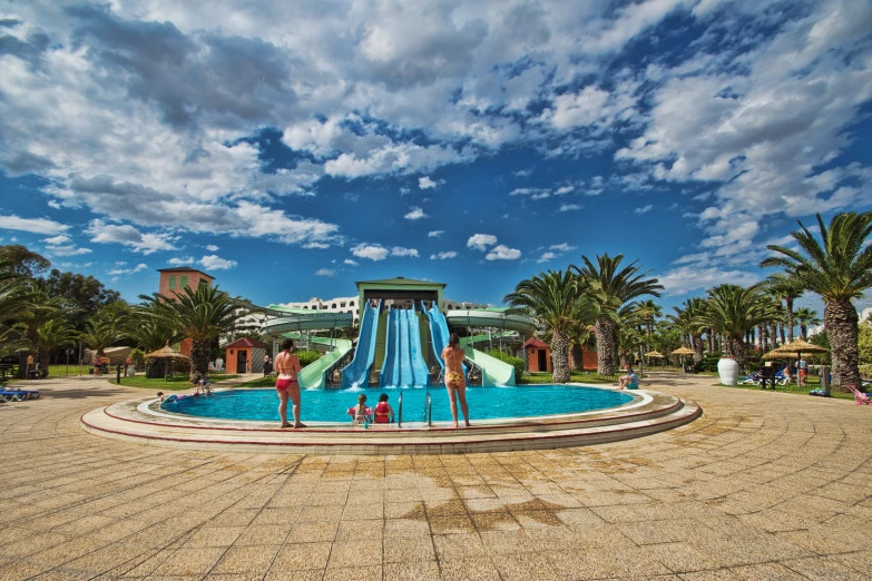 a group of people stand around a blue water slide