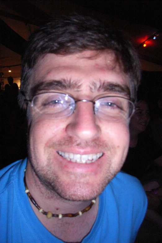 a smiling man wearing glasses while standing in front of people