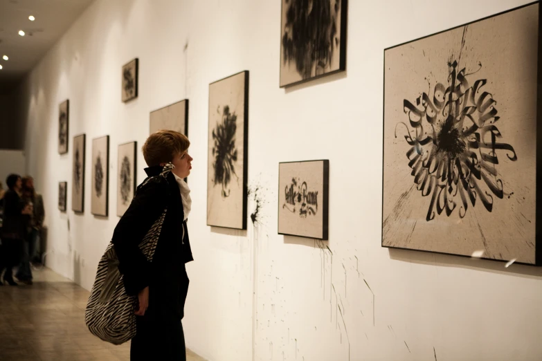 a woman standing in a museum looking at various art hanging on the wall