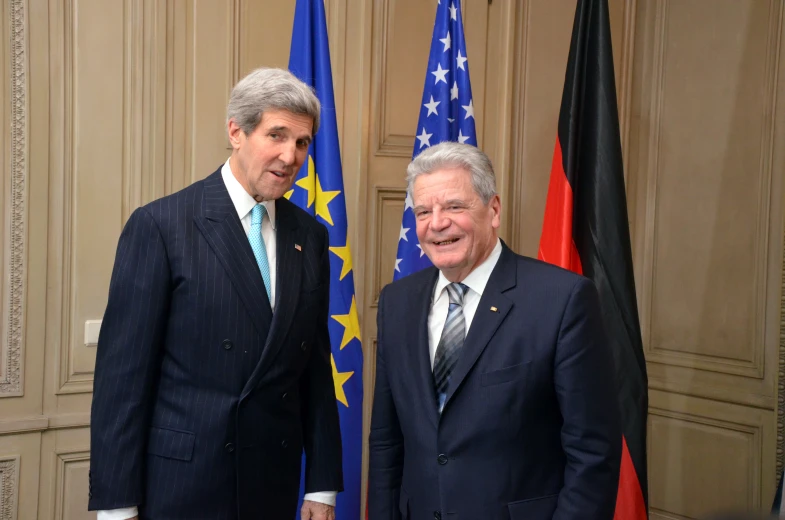 two men in suits standing next to each other in front of flags