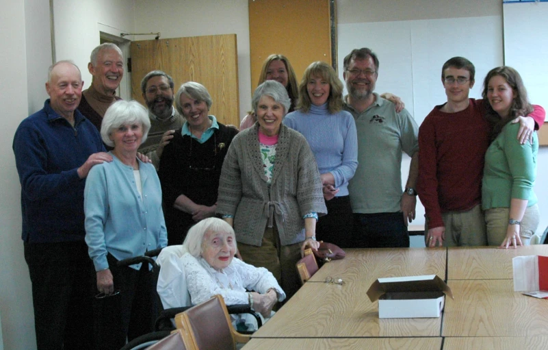 a group of older people standing and sitting around a conference table