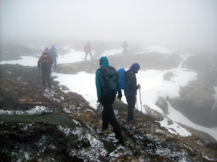 people hiking up hill in fog and snow