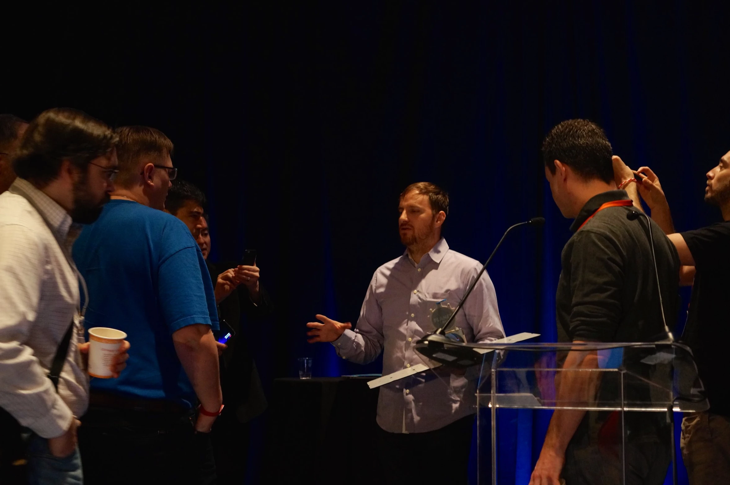 two men talking and one wearing a white shirt is holding a microphone