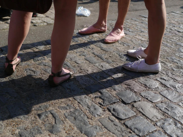 several people in pink slip on shoes standing on cobblestones