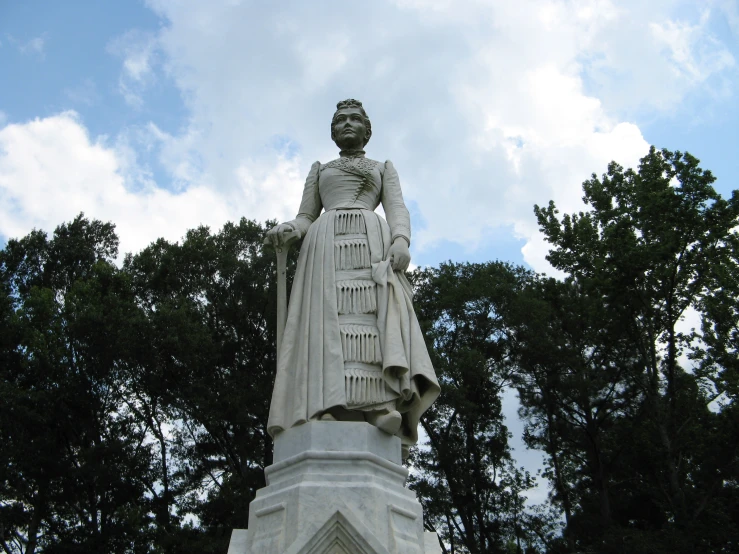 a woman is standing in front of trees on the top of a stone statue