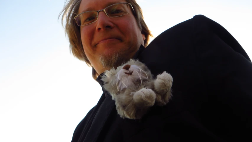 a man with glasses holds a cat that is laying on his shoulder
