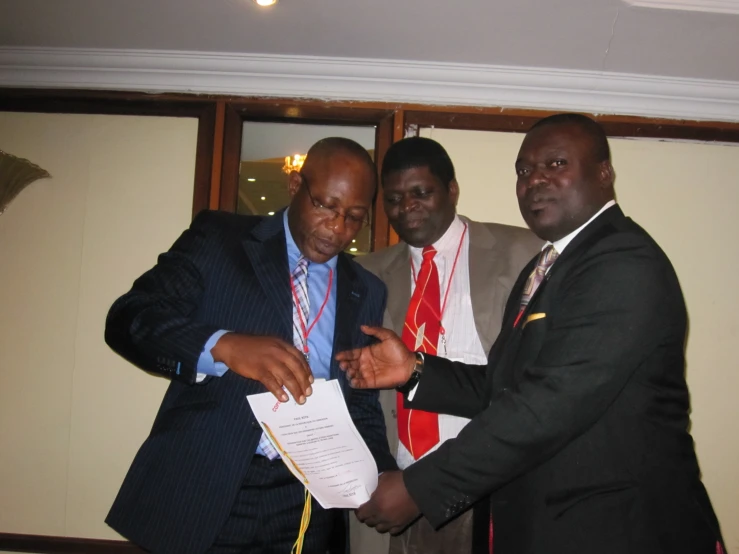 three men wearing suits holding papers and wearing ties