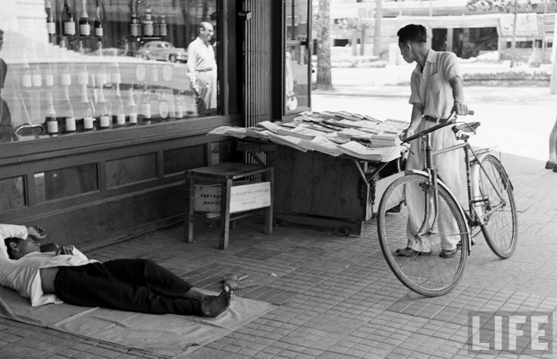 a person laying on the ground next to a bicycle near another person sitting on a sidewalk