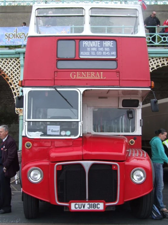 a red double decker bus parked in front of a bridge