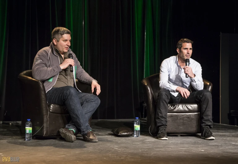 two men sitting on chairs in front of a stage