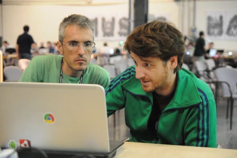 two men sit in front of a laptop, both looking at the same screen