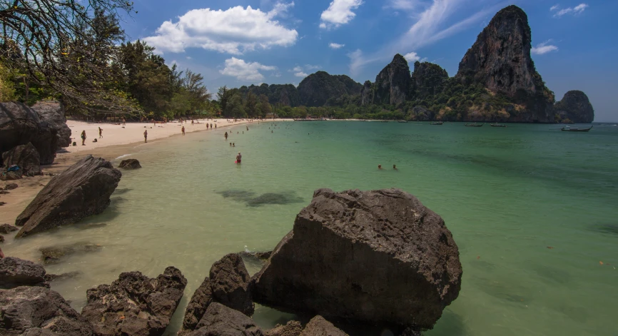 people are walking on the beach towards rocks