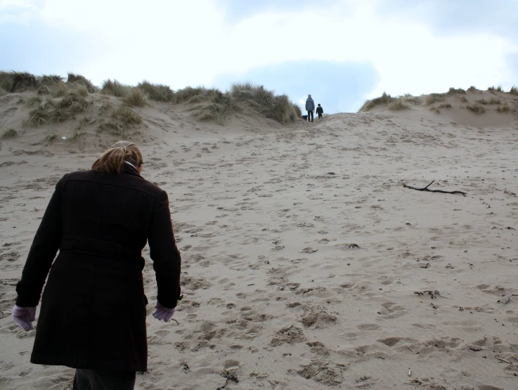 a woman with her back to the camera walking down a sandy hill