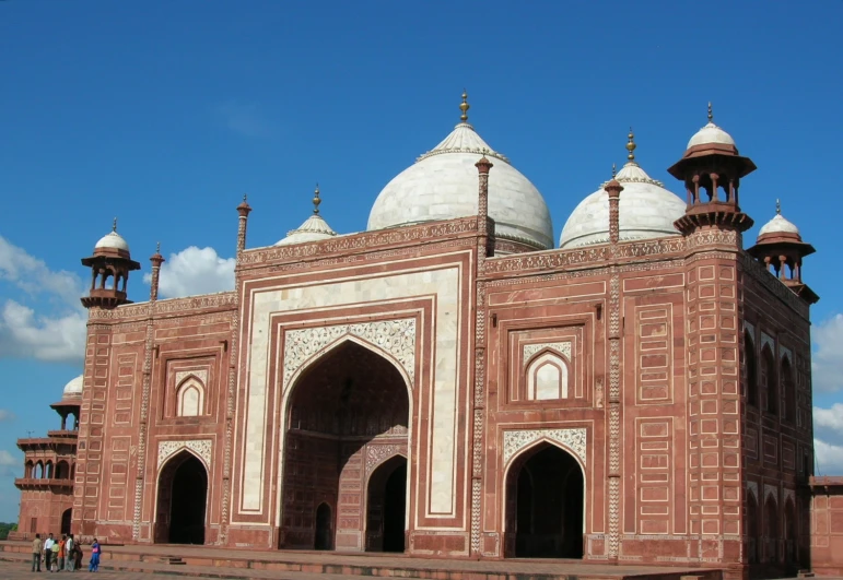 people walk next to a white and red building with domes