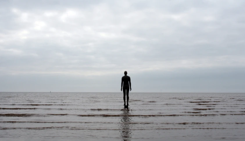 a person standing in the water alone on a cloudy day