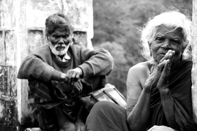 an elderly woman and younger man sitting against a wall