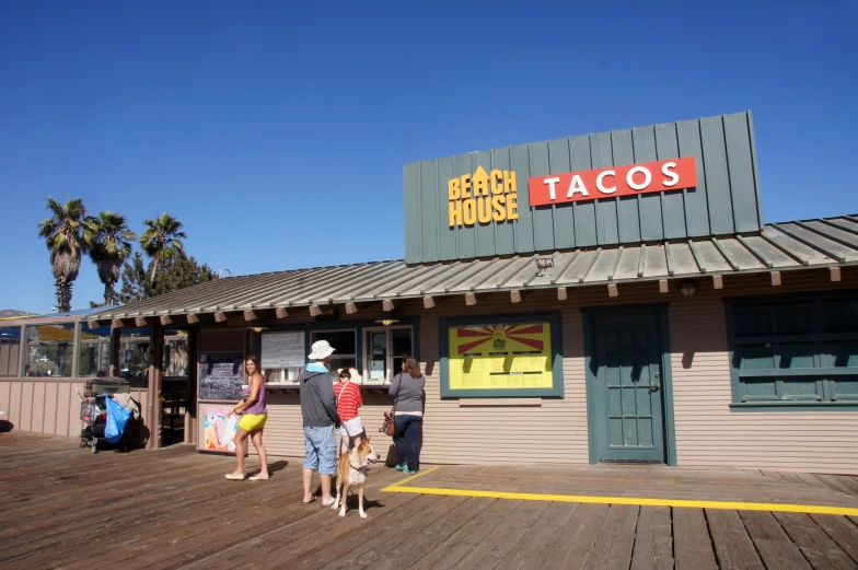 people are walking outside of a taco stand with a large sign