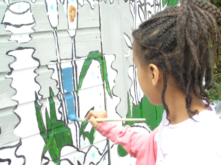 a little girl drawing on a wall with a brush