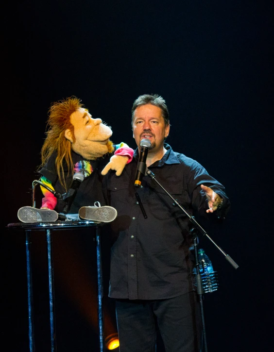 a man speaking at a podium while a puppet is holding a microphone