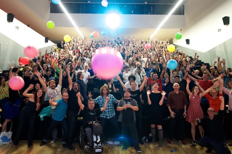 people standing and sitting in an auditorium with their hands raised up