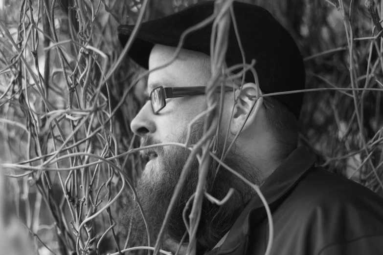 a man with a beard and glasses standing behind the nches of a tree