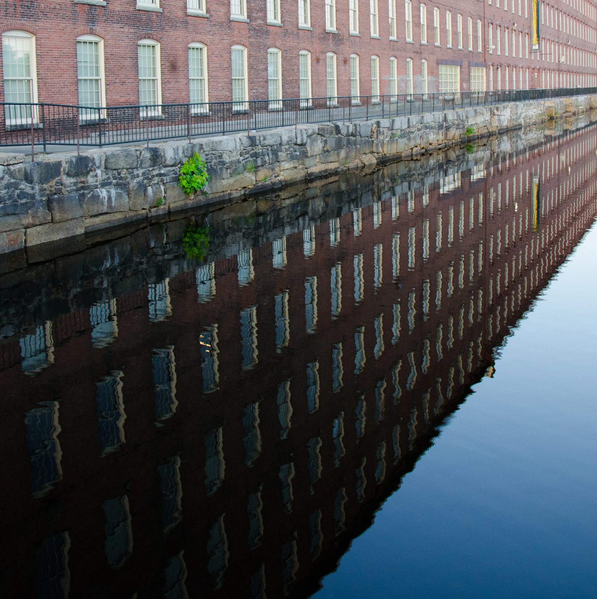 a long line of brick buildings reflect on a calm canal