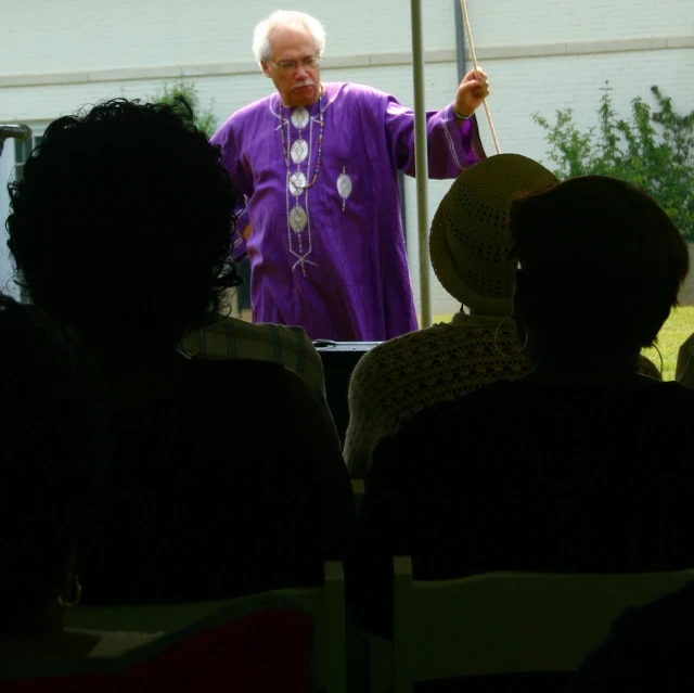 an old man in a purple robe speaking to people