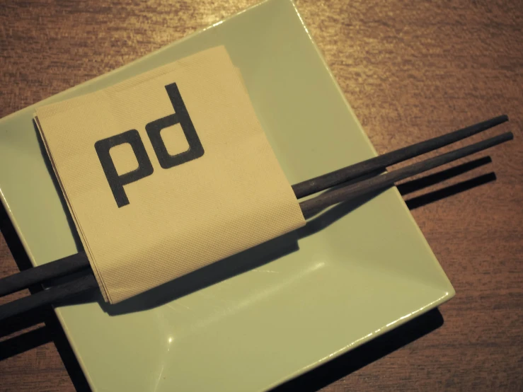 a square plate topped with black chop sticks and a napkin that says po