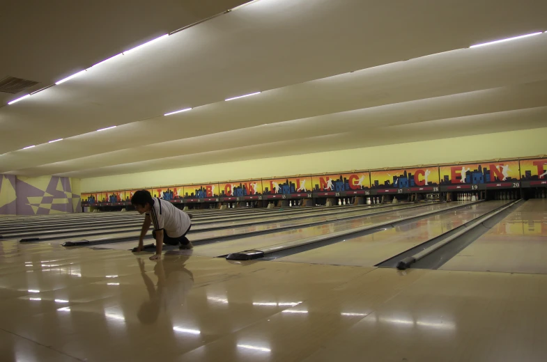 man kneeling down next to bowling lanes in a gymnasium