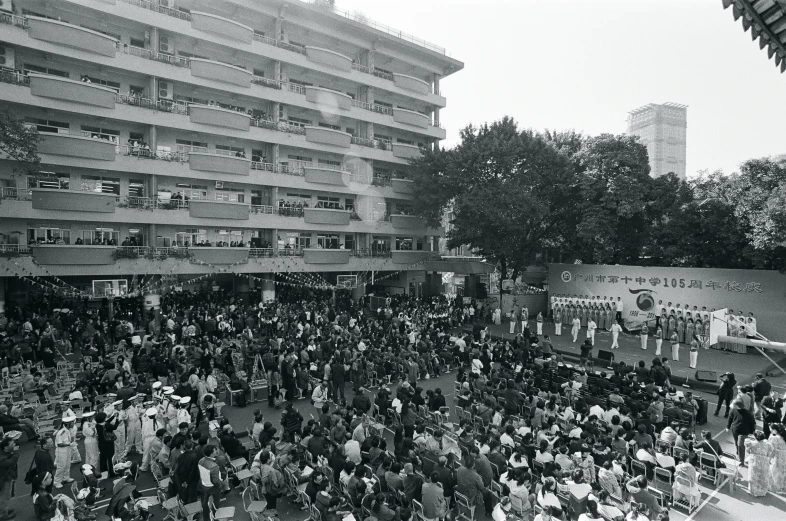 an outdoor gathering in front of the building with people milling about