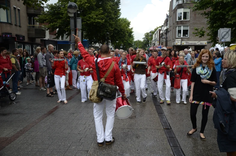 a parade with men in red jackets and white pants walking along the street