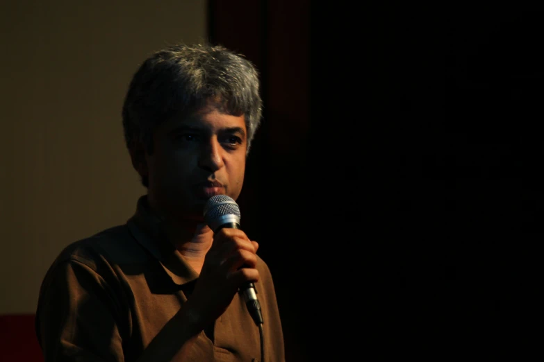 a man in a brown shirt is talking into a microphone
