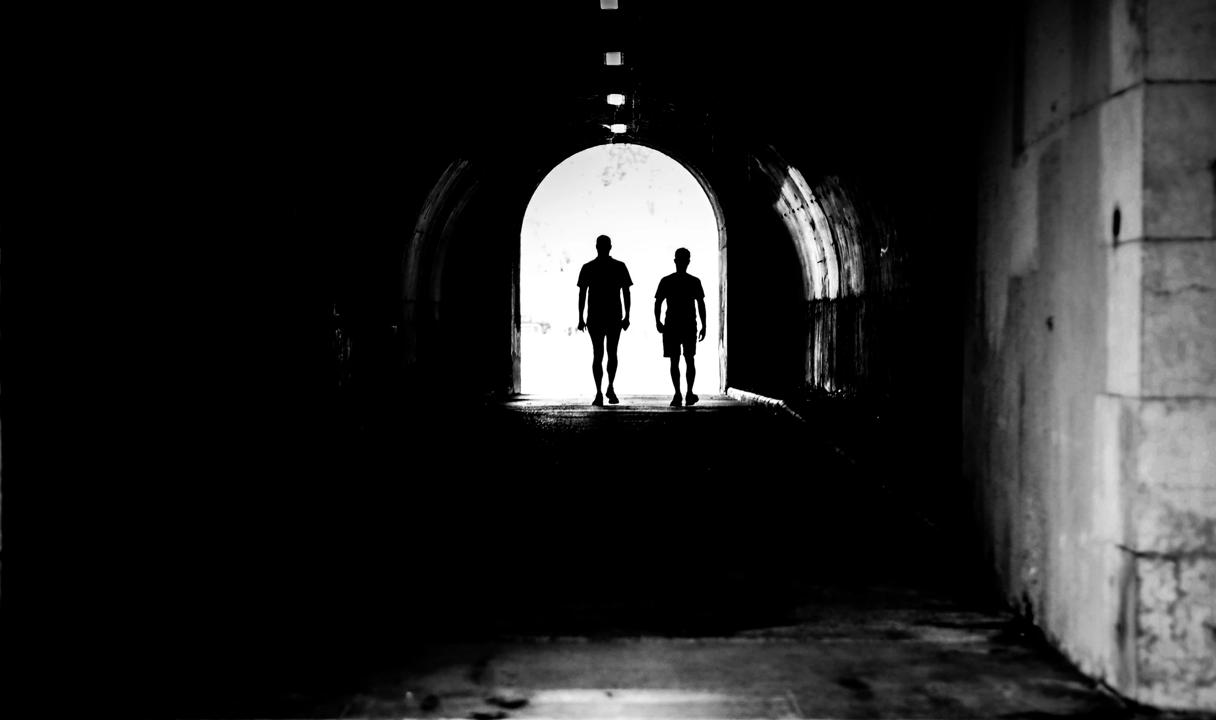 two silhouettes are standing in the middle of a dark tunnel