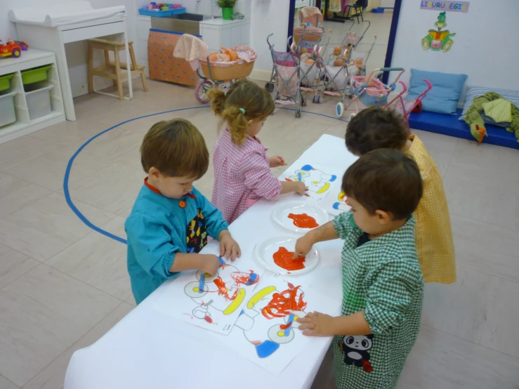 three children sit at a table and are painting the pieces