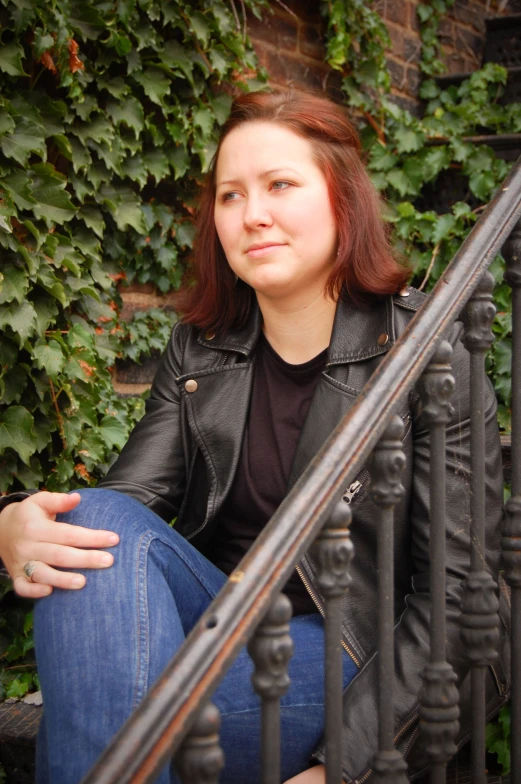 a pretty young woman in black jacket and jeans sitting down