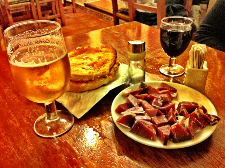 plates of food on a wooden table next to beer glasses