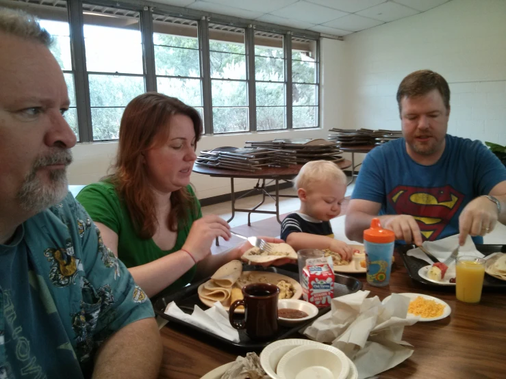 two men, a woman and a child are sitting at the table eating