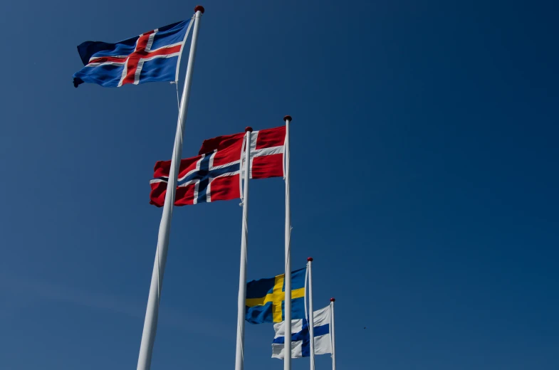 many different flags fly in a clear blue sky