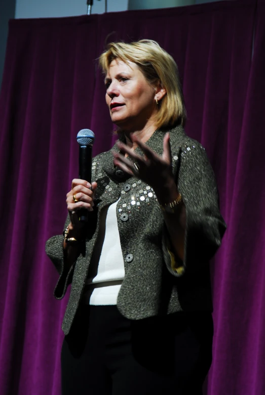 a woman holding a microphone in front of purple curtains