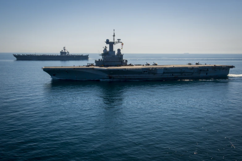 an aircraft carrier is being maneuvered on a large body of water with three ships in the background