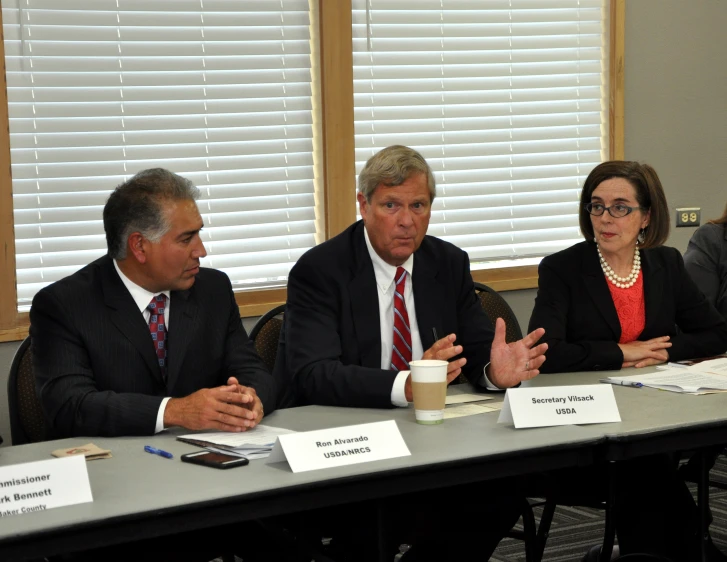 three men and a woman sitting at a table talking