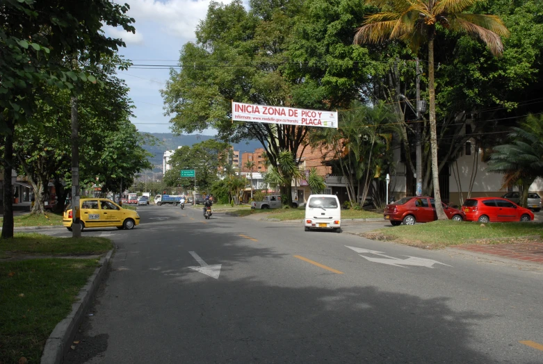 a car, moped and three wheeler drive down a street in a town