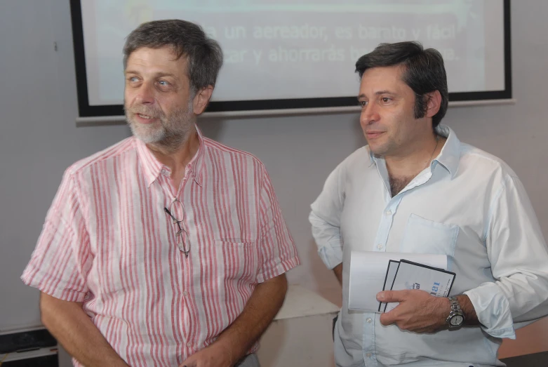 two men smiling and standing in front of a projector screen