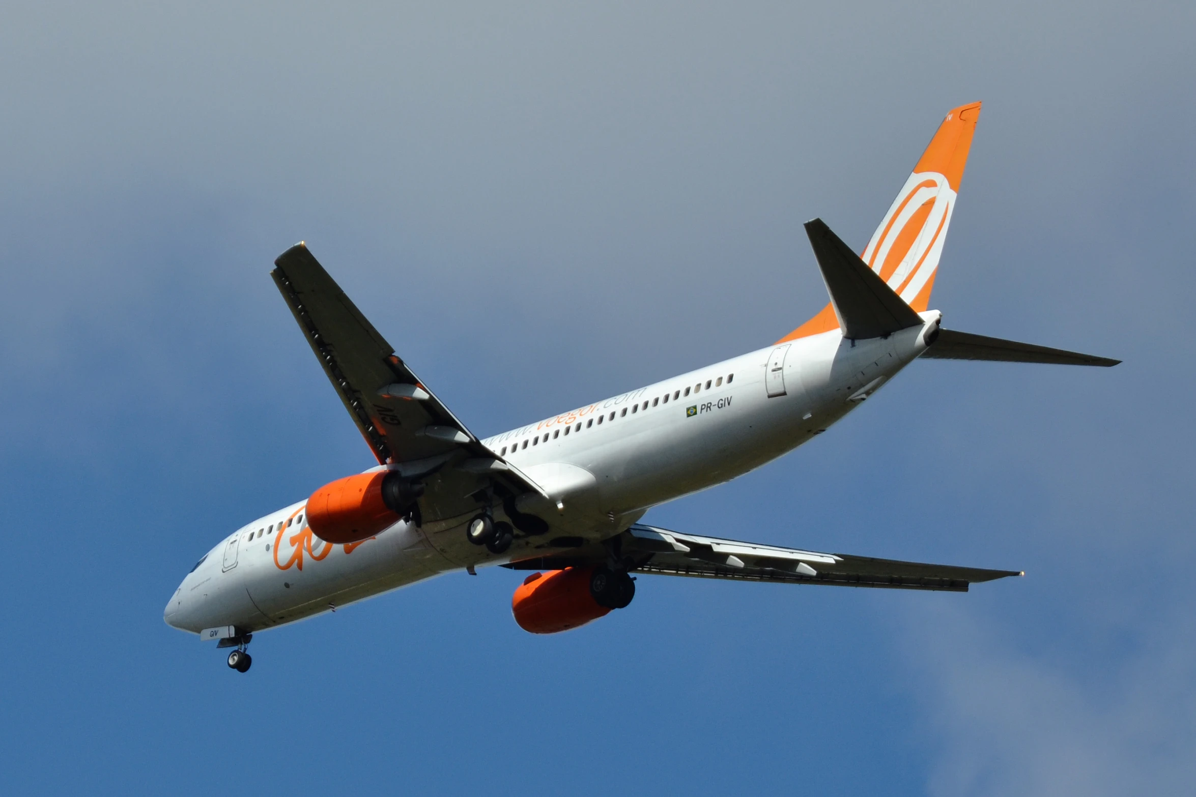 a white plane with an orange and blue trim flying in the sky