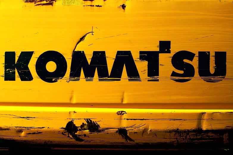 there is the words komatsu written on the side of a yellow wall