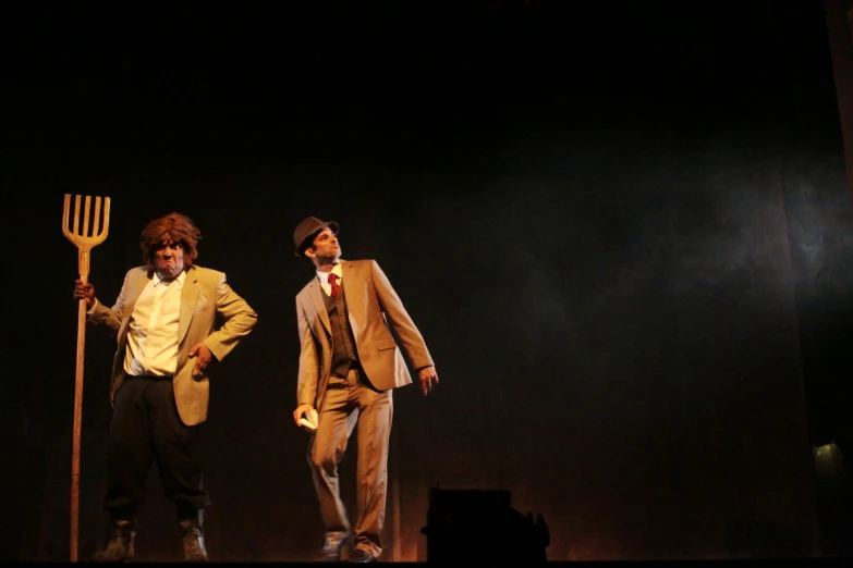 two men in costume posing on stage with a long wooden cane