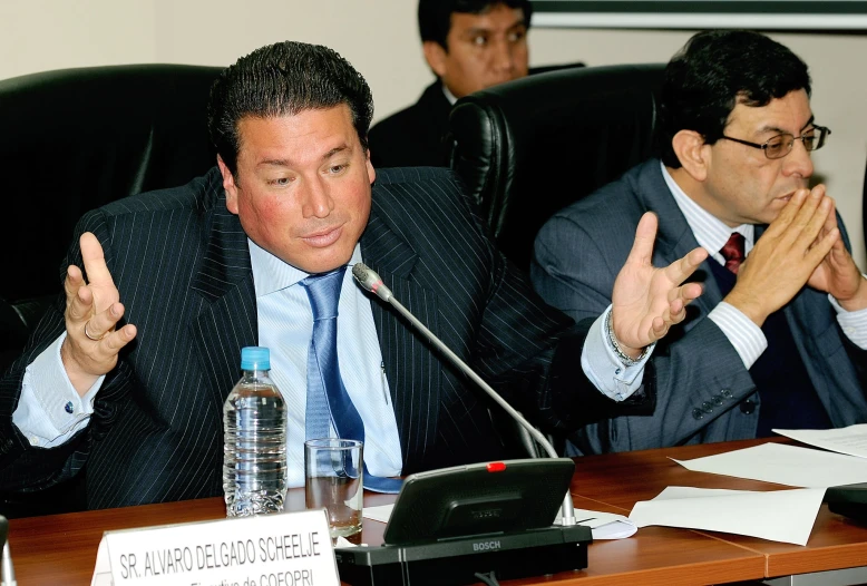 two people sitting in a room at a table clapping with their hands up