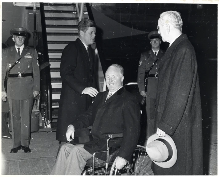 an older man in a wheel chair in front of two men