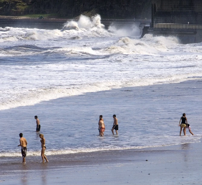 several people walking along a beach and two standing in the ocean